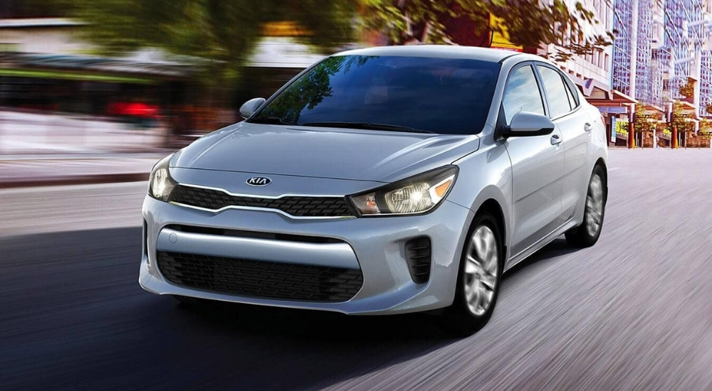 A silver 2020 Kia Rio is shown driving on a city street.