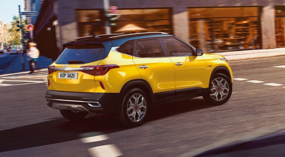 A yellow 2021 Kia Seltos is shown driving through an intersection.