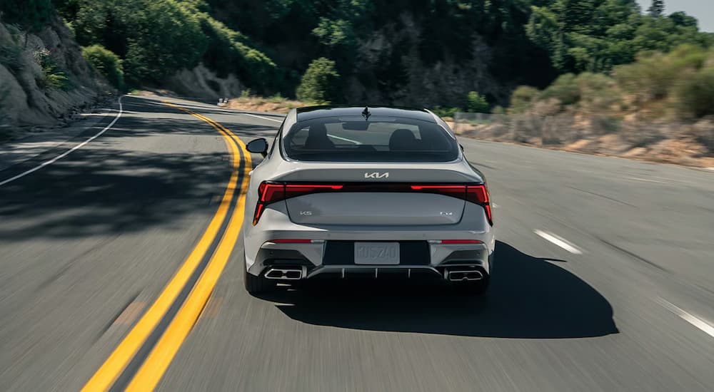 Rear of a grey 2026 Kia K5 for sale driving on a winding road