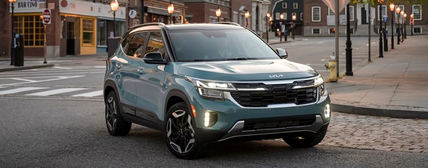 A blue 2025 Kia Seltos SX driving downtown to visit a Kia dealer.