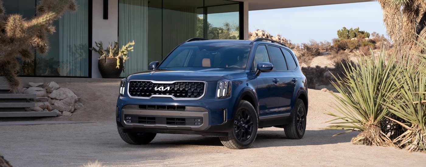 A blue 2024 Kia Telluride parked near a home.